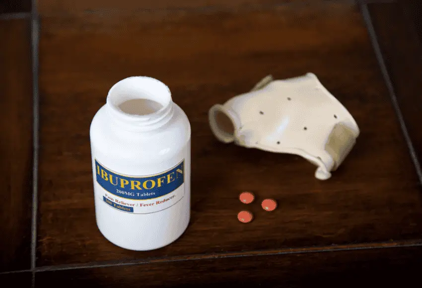 A bottle of ibuprofen tablets spilled on a table next to a dog cone.